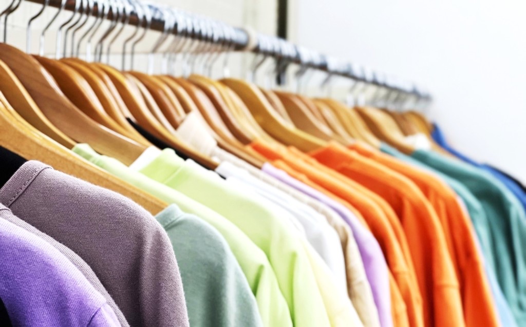 パープルやグリーン、オレンジなどカラフルなTシャツが木製ハンガーに掛けられてラックに並んでいるおしゃれな写真
