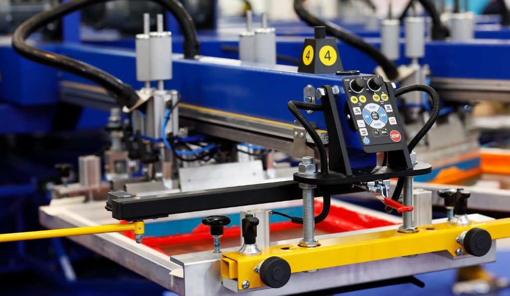 クラスTシャツのプリントに使われるシルクスクリーン印刷機のクローズアップ写真で版と操作パネルが見える