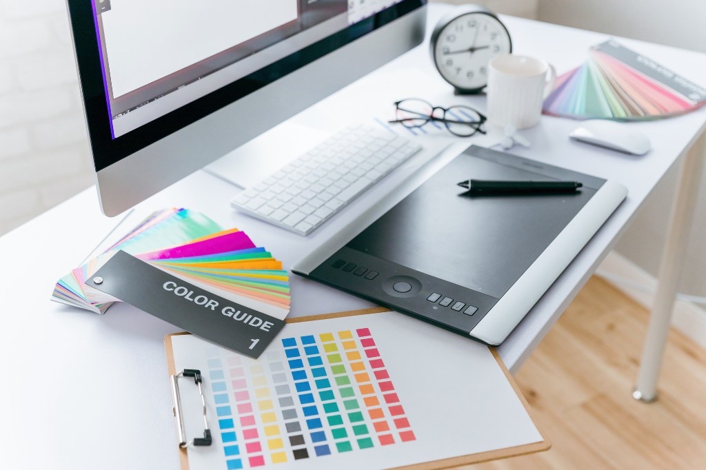 グラフィックデザイナーのデスク。大きなモニター、ペンタブレット、カラーガイド、キーボードが写っており、入稿データを作成するための作業環境のイメージです。