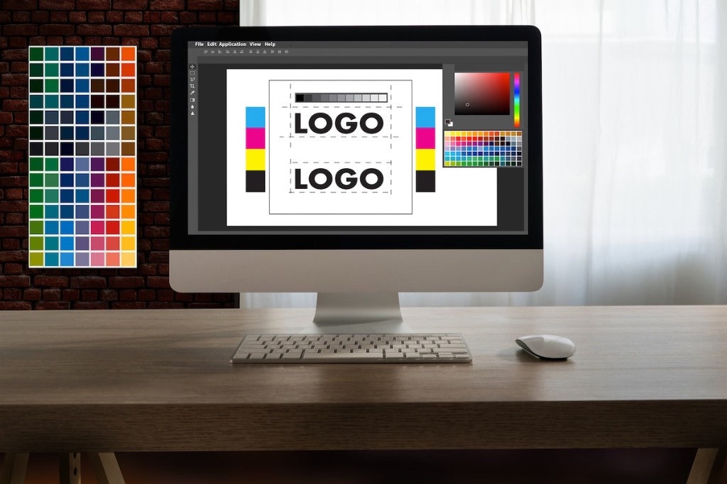 iMacでロゴデザインやCMYKカラーを確認しているデザインワークスペース。オリジナルグッズの入稿データ準備のイメージが伝わる。