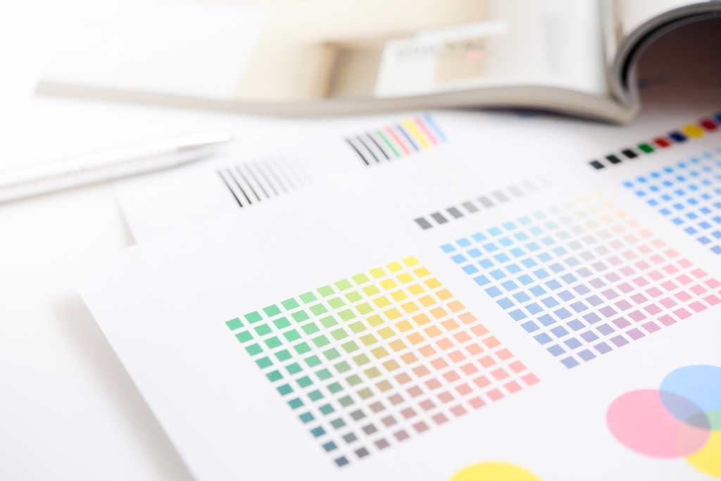 緑から黄・オレンジ、青から紫まで色相が並んだカラースウォッチとCMYKの校正バーが写ったデザイン作業の写真