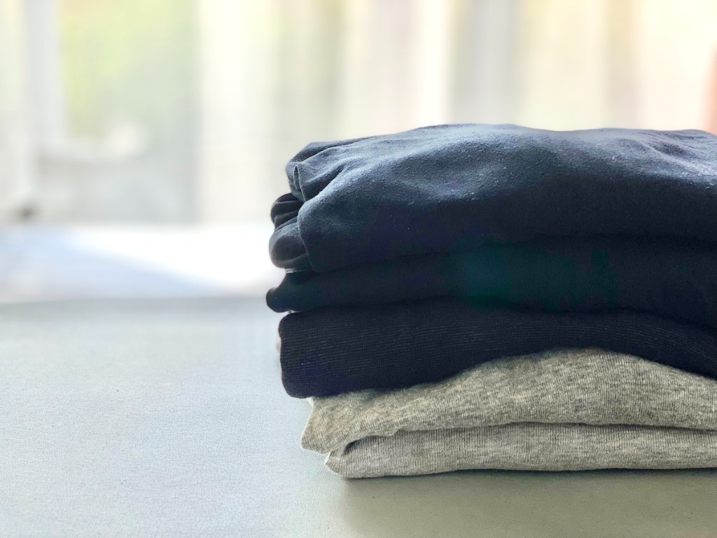 丁寧にたたんだTシャツやカジュアルウェアの山。プリント面を内側にして収納する習慣が伝わる。