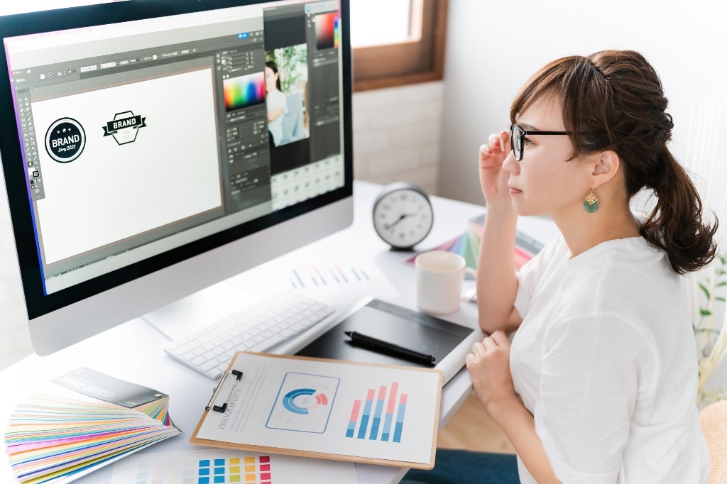 パソコンの画面でデザインソフトを使いオリジナルグッズのロゴデータを制作する女性デザイナー。解像度やカラーモードの事前チェックが仕上がり品質を左右する
