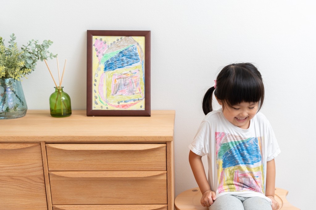 子どもが描いたカラフルな絵をそのままプリントしたオリジナルTシャツを着て笑顔の女の子。1枚からでもフルカラーで高品質なオリジナルTシャツが作れる時代になった